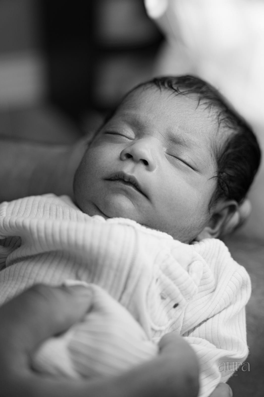 A newborn asleep in a soft white wrap, in black and white