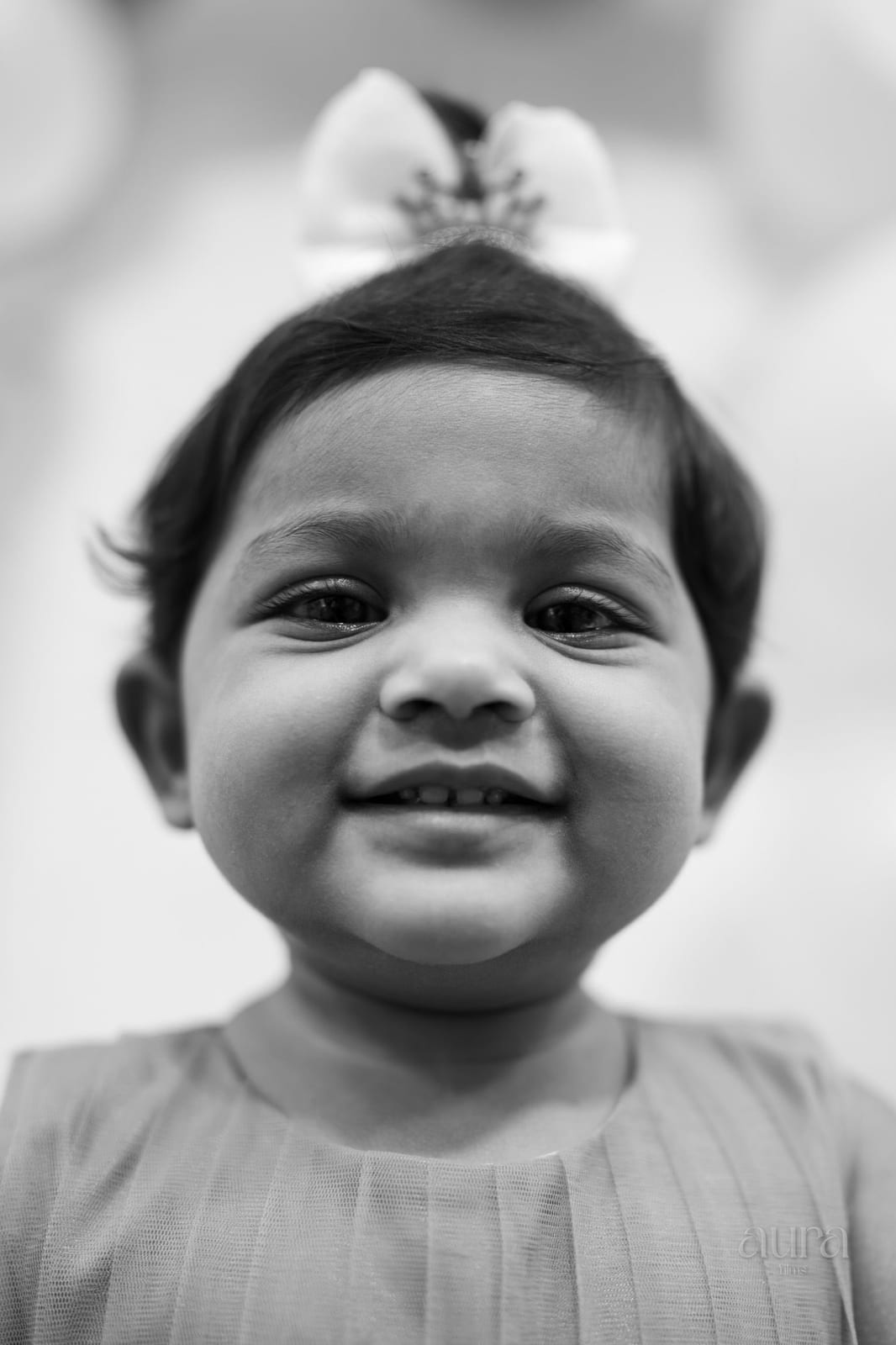 A toddler with a bow in her hair grins at the camera, in black and white