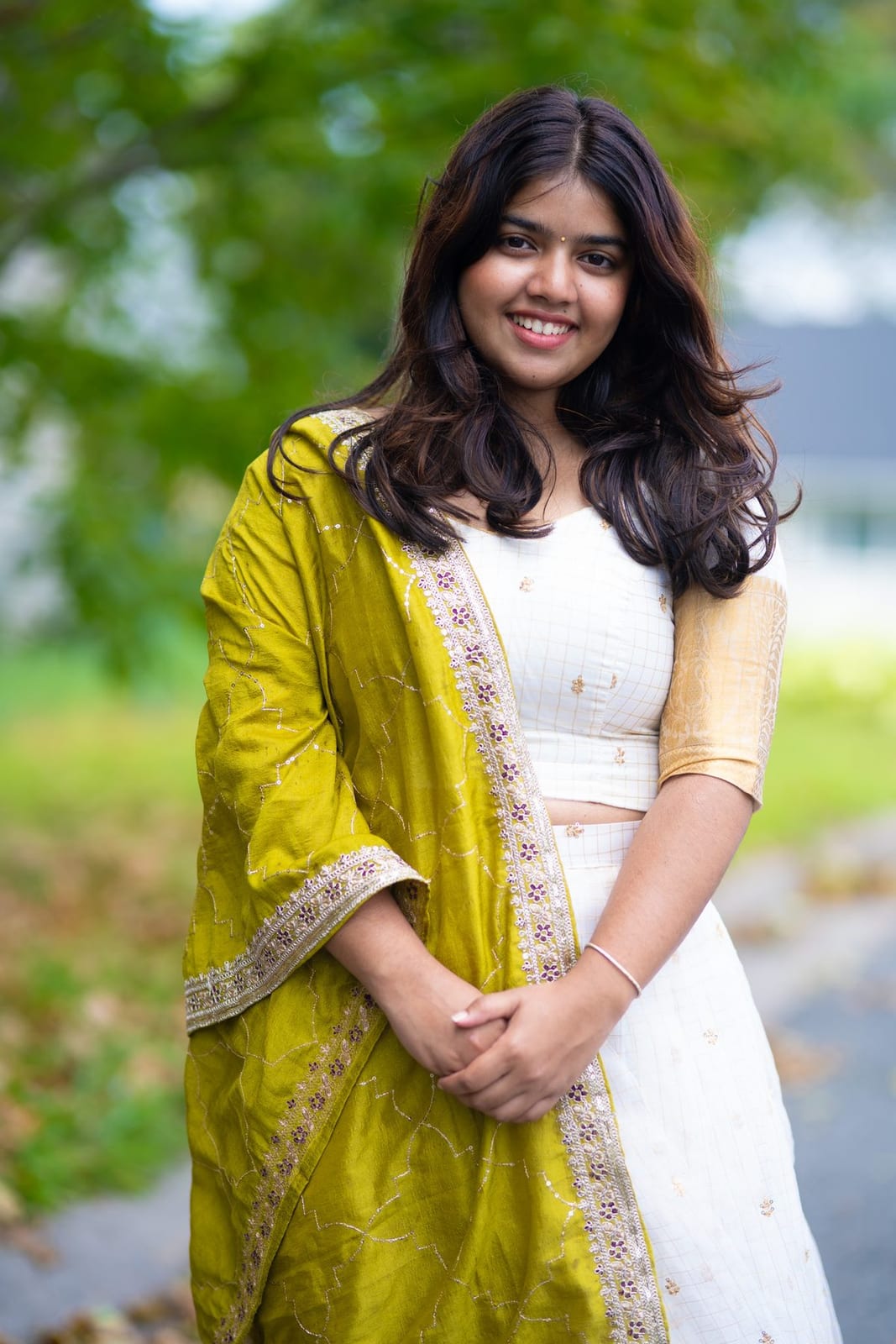 A woman in a mustard dupatta smiles among autumn trees