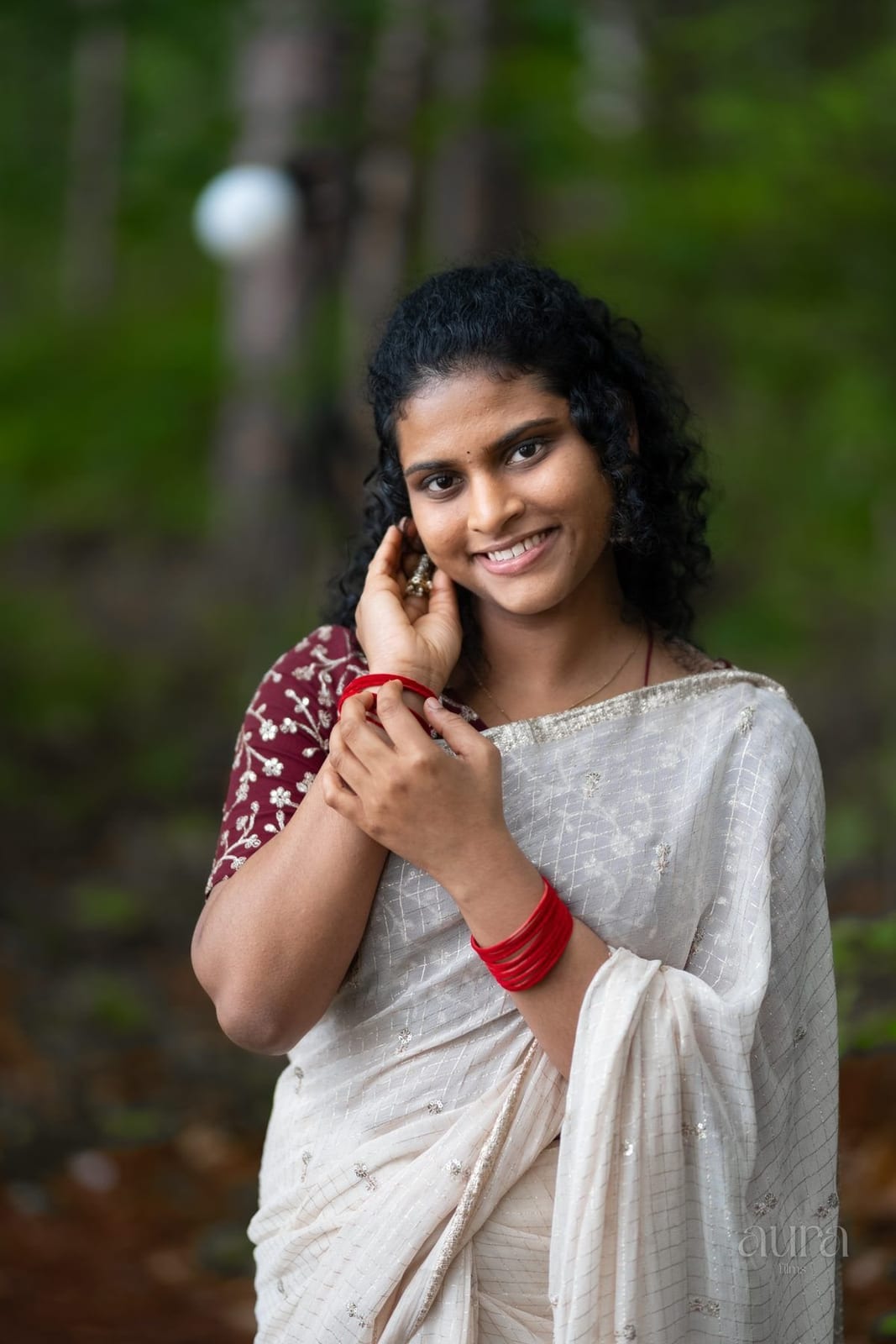 A woman in a white embroidered saree and red bangles, smiling softly