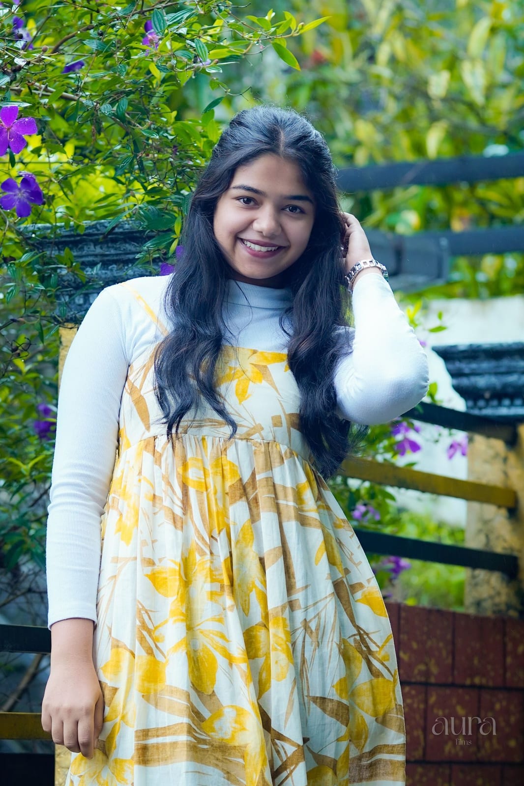 A woman in a white cardigan and yellow dress beside a garden