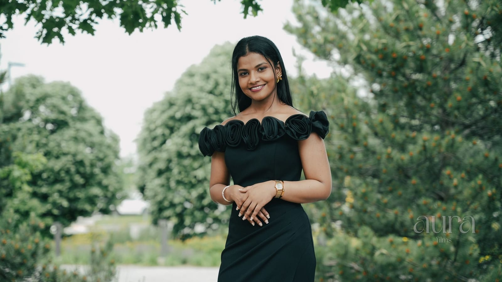 A woman in a black off-shoulder dress in front of summer greenery