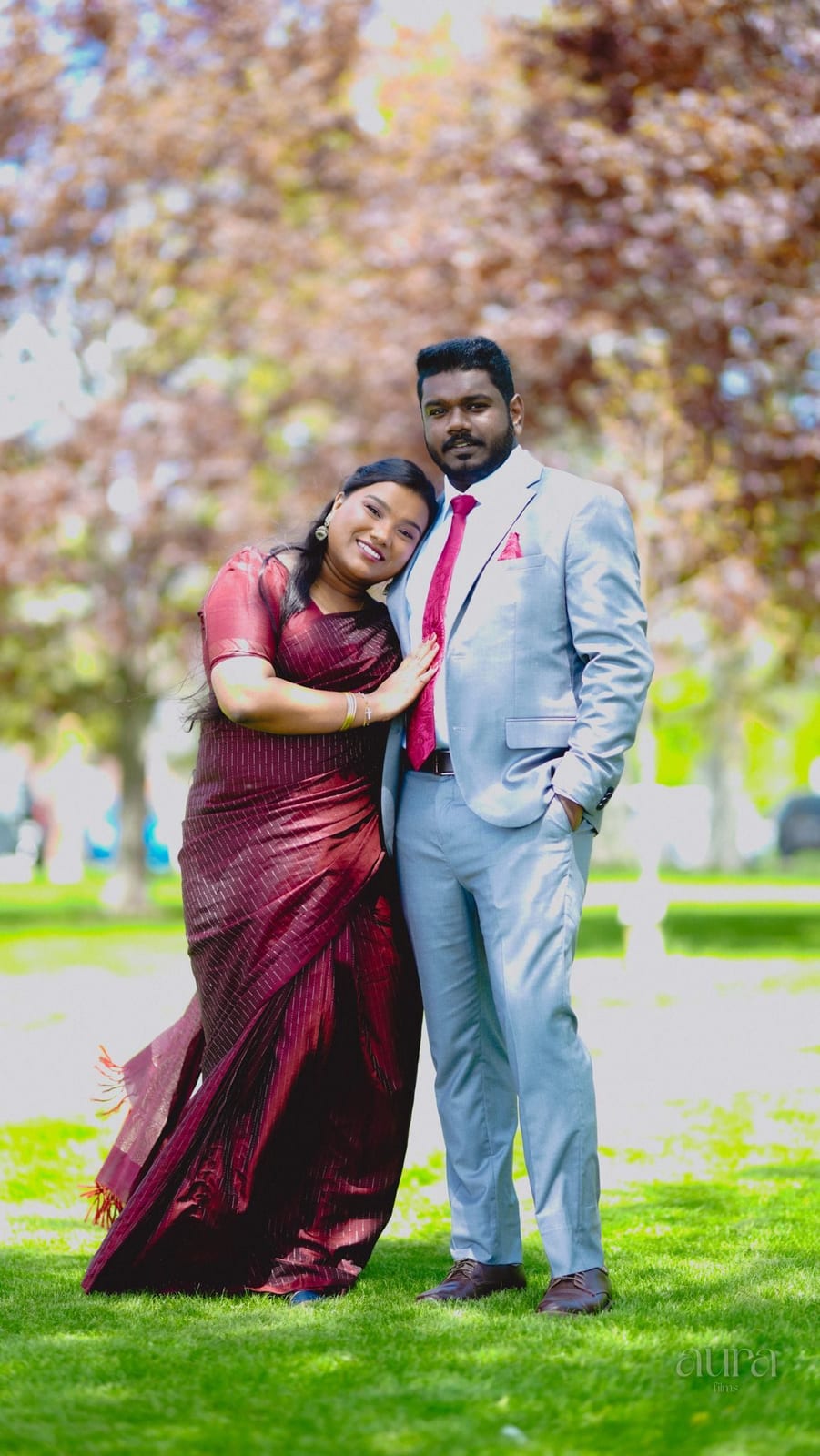 A bride in a deep red saree leans on her groom under spring blossom