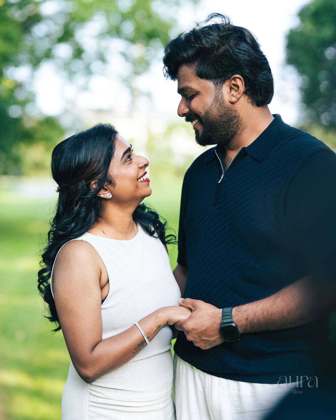 A couple hold hands and laugh together in a sunlit park